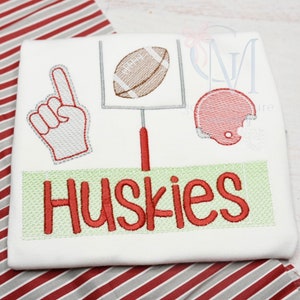 May include: White onesie with red embroidered football, helmet, and hand with a raised finger. The onesie also has a green and white banner with the word "Huskies" in red.