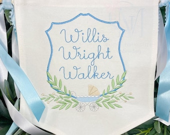 May include: A white banner with blue ribbon ties, featuring an embroidered blue shield with the text "Willis Wright Walker" and a small blue baby carriage with green leaves.