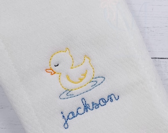 May include: White embroidered burp cloth with a yellow rubber ducky in a blue tub and the name "Jackson" embroidered in blue.