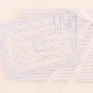 May include: A light blue embroidered birth announcement with the name "Davis Ivey Coule", date, time, weight (9 lbs 5 oz), and length (23 inches). The announcement is on a light blue striped background with white lace.