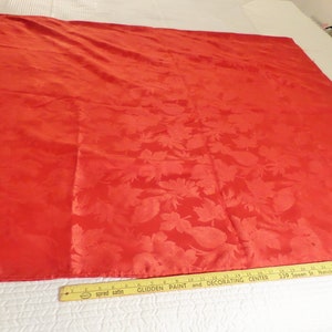 May include: A large, rectangular red satin fabric with a floral pattern. The fabric is spread out on a white surface. A ruler is placed along the bottom edge. The fabric is approximately 60 inches wide.
