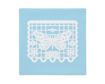 Butterfly decorative pillow sham 18"x18" in baby blue with white papel picado from the book A Is For Alpaca And Amigos © by Lisa Osterman