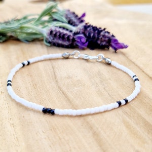 May include: A white beaded bracelet with black accents. The bracelet has a silver clasp.