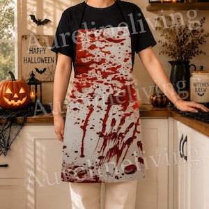 May include: A white kitchen apron featuring a graphic print of red blood splatters and drips across the entire front surface. The apron has black neck and waist ties and is worn over a black short-sleeved t-shirt and light-colored pants.