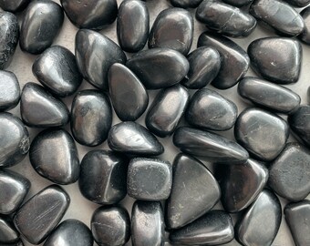 May include: A collection of polished, black stones with a smooth, reflective surface. The stones vary in size and shape, ranging from rounded to oblong. The overall appearance is dark and glossy, with subtle variations in tone and texture.