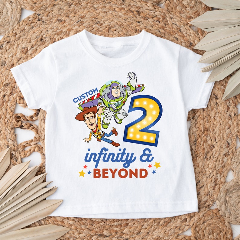 May include: White t-shirt with a graphic of Woody and Buzz Lightyear from Toy Story. The graphic includes the number "2" with light bulbs around it and the text "infinity & BEYOND".