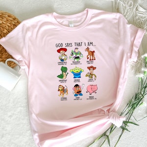 Peut inclure: T-shirt rose avec un graphique de personnages de Toy Story et des versets bibliques qui disent "Dieu dit que je suis..." Les personnages incluent Woody, Buzz l'&Eacute;clair, Rex, Jessie, Hamm, Bullseye, Slinky Dog et M. Patate.