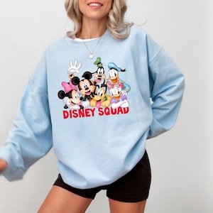 Puede incluir: Sudadera azul claro con un gr&aacute;fico de personajes de Disney, incluyendo Mickey Mouse, Minnie Mouse, Goofy, Donald Duck y Pluto. Las palabras "DISNEY SQUAD" est&aacute;n impresas en rojo en la parte inferior del gr&aacute;fico.