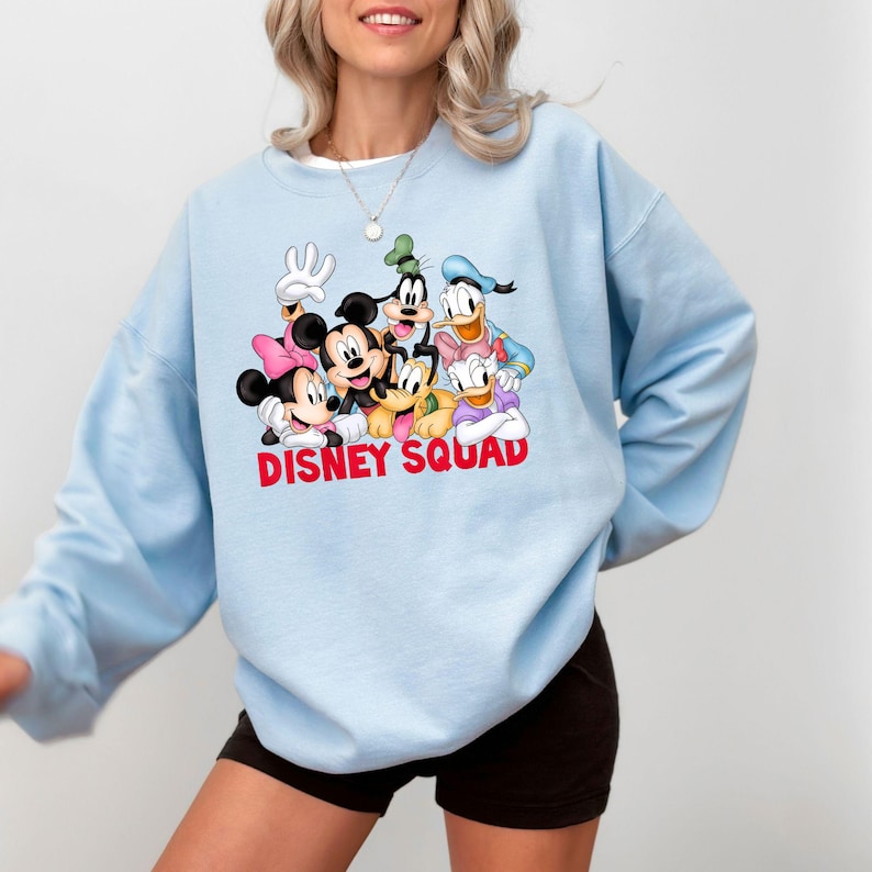 Puede incluir: Sudadera azul claro con un gr&aacute;fico de personajes de Disney, incluyendo Mickey Mouse, Minnie Mouse, Goofy, Donald Duck y Pluto. Las palabras "DISNEY SQUAD" est&aacute;n impresas en rojo en la parte inferior del gr&aacute;fico.
