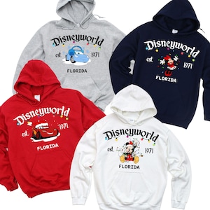May include: Four hooded sweatshirts in red, white, navy blue, and gray. Each sweatshirt features the "Disneyworld" logo with a character graphic and the text "est. 1971 FLORIDA". The sweatshirts have a front pocket and a drawstring hood.