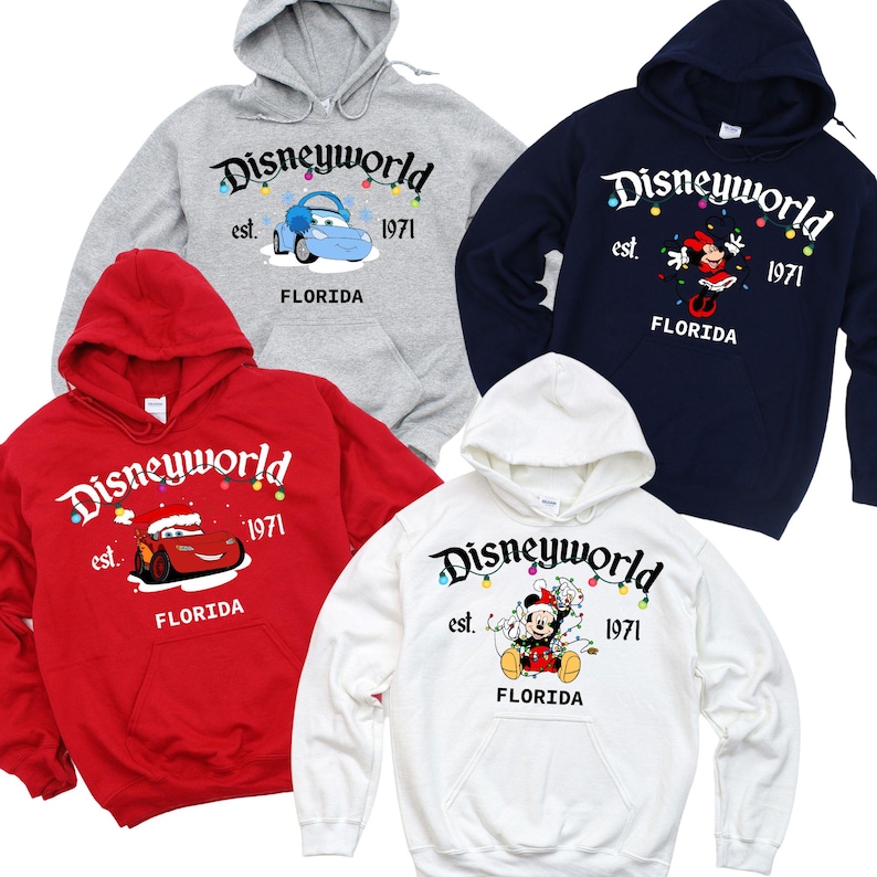 May include: Four hooded sweatshirts in red, white, navy blue, and gray. Each sweatshirt features the "Disneyworld" logo with a character graphic and the text "est. 1971 FLORIDA". The sweatshirts have a front pocket and a drawstring hood.