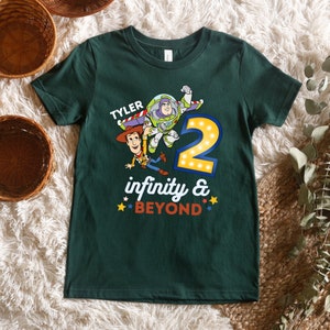 May include: A green t-shirt with a graphic of Woody and Buzz Lightyear from Toy Story. The graphic includes the number 2 with lights around it and the text "TYLER infinity & BEYOND".