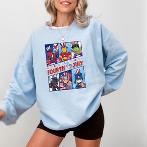 May include: Light blue sweatshirt with a graphic of Disney characters wearing red, white, and blue patriotic hats. The text "Disney FOURTH OF JULY" is printed on the sweatshirt.