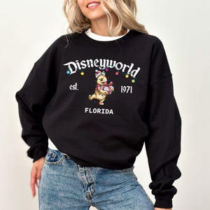 May include: Black sweatshirt with the text "Disneyworld est. 1971 FLORIDA". The sweatshirt features a graphic of Winnie the Pooh holding a gift and wearing a Santa hat, with colorful Christmas lights.