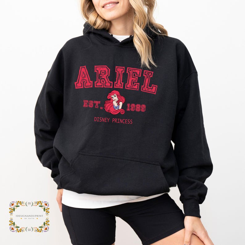 May include: Black hooded sweatshirt featuring the name "ARIEL" in red block letters. Underneath, the text reads "EST. 1989 DISNEY PRINCESS" in red. A graphic of Ariel is in the center of the text.