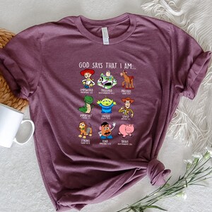 Peut inclure: Un t-shirt violet avec un graphique de personnages de Toy Story et des versets bibliques. Le texte dit "Dieu dit que je suis..." avec chaque personnage repr&eacute;sentant un verset diff&eacute;rent.