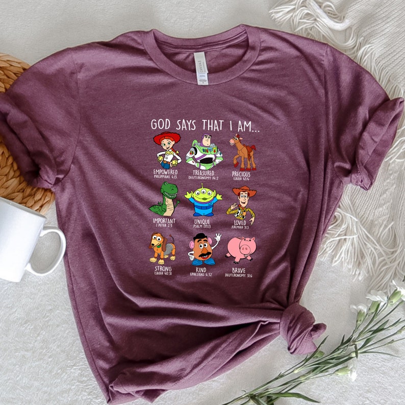 Peut inclure: Un t-shirt violet avec un graphique de personnages de Toy Story et des versets bibliques. Le texte dit "Dieu dit que je suis..." avec chaque personnage repr&eacute;sentant un verset diff&eacute;rent.