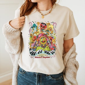 May include: A beige t-shirt with a colorful graphic of the Muppets playing instruments. The graphic includes the text "Dr. Teeth & The Electric Mayhem".