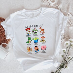 Peut inclure: T-shirt blanc avec un graphique de personnages de Toy Story et le texte "GOD SAYS THAT I AM..." avec des versets bibliques sous chaque personnage.