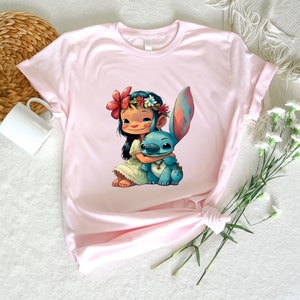 May include: A pink t-shirt with a cartoon image of Lilo from Lilo & Stitch, wearing a flower crown and hugging Stitch.