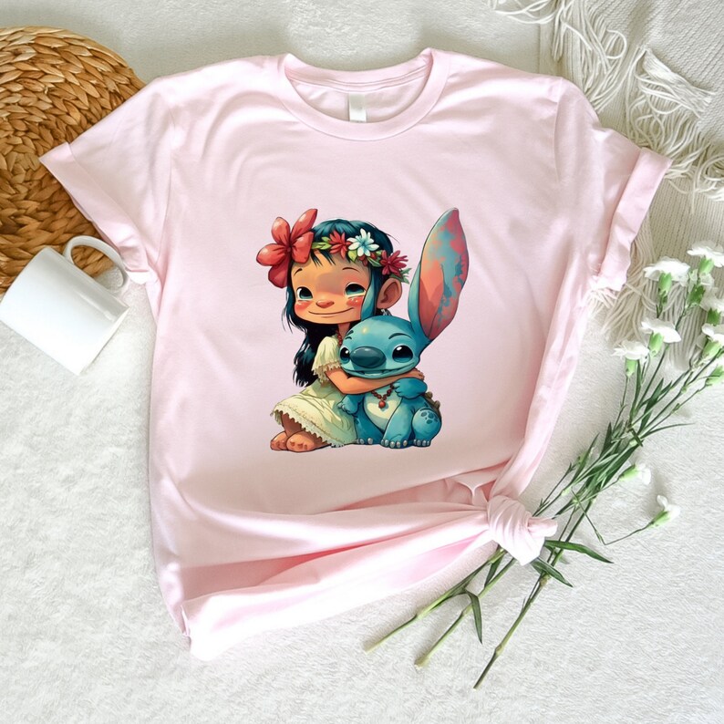 May include: A pink t-shirt with a cartoon image of Lilo from Lilo & Stitch, wearing a flower crown and hugging Stitch.