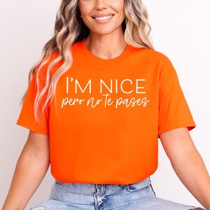 May include: A bright orange short-sleeved t-shirt featuring the text I'M NICE in a bold, white sans-serif font, followed by the text pero no Te pases in a white, cursive script font centered on the chest of the garment.