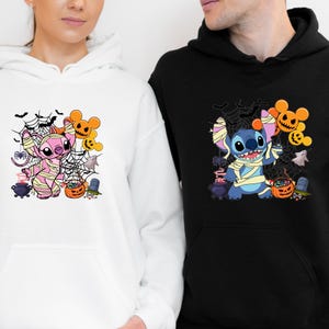 May include: White and black hoodies featuring Halloween-themed Stitch characters. The white hoodie has a pink mummy Stitch, while the black hoodie has a blue mummy Stitch. Both designs include pumpkins, spiderwebs, and bats.