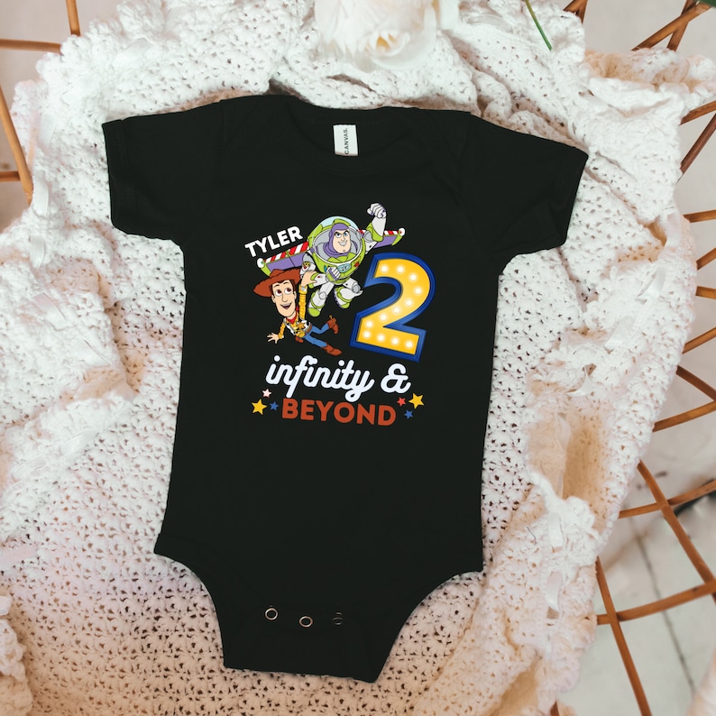 May include: Black bodysuit with a Toy Story theme. It features Woody and Buzz Lightyear characters, a number 2, and the text "TYLER infinity & BEYOND".