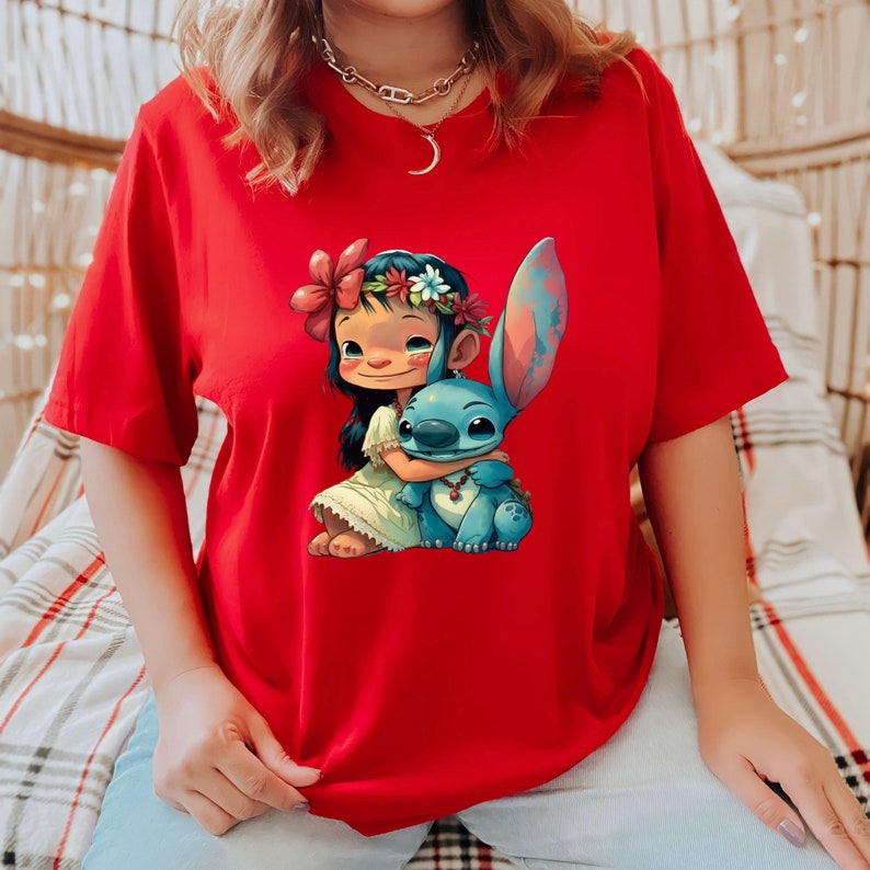 May include: Red t-shirt with a graphic print of a girl with a flower crown hugging a blue Stitch character from Lilo & Stitch.