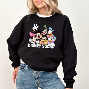 Puede incluir: Sudadera negra con un gr&aacute;fico colorido de personajes de Disney, incluyendo Mickey Mouse, Minnie Mouse, Goofy, Pato Donald y Daisy. El texto "DISNEY SQUAD" est&aacute; impreso debajo. La sudadera tiene cuello redondo y mangas largas.