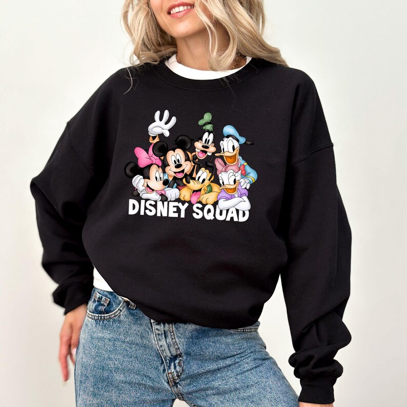 Puede incluir: Sudadera negra con un gr&aacute;fico colorido de personajes de Disney, incluyendo Mickey Mouse, Minnie Mouse, Goofy, Pato Donald y Daisy. El texto "DISNEY SQUAD" est&aacute; impreso debajo. La sudadera tiene cuello redondo y mangas largas.