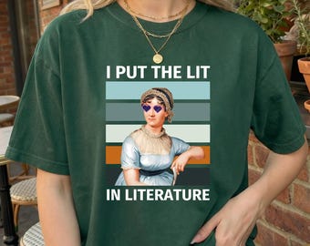 May include: A dark green short-sleeve t-shirt featuring a graphic of a historical figure wearing heart-shaped sunglasses. The text "I PUT THE LIT IN LITERATURE" is printed above and below the figure, set against a background of horizontal stripes.