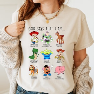Peut inclure: Un t-shirt beige avec un graphique de personnages de Toy Story et des versets bibliques. Le texte dit "Dieu dit que je suis..." et liste les noms des personnages et les versets bibliques.