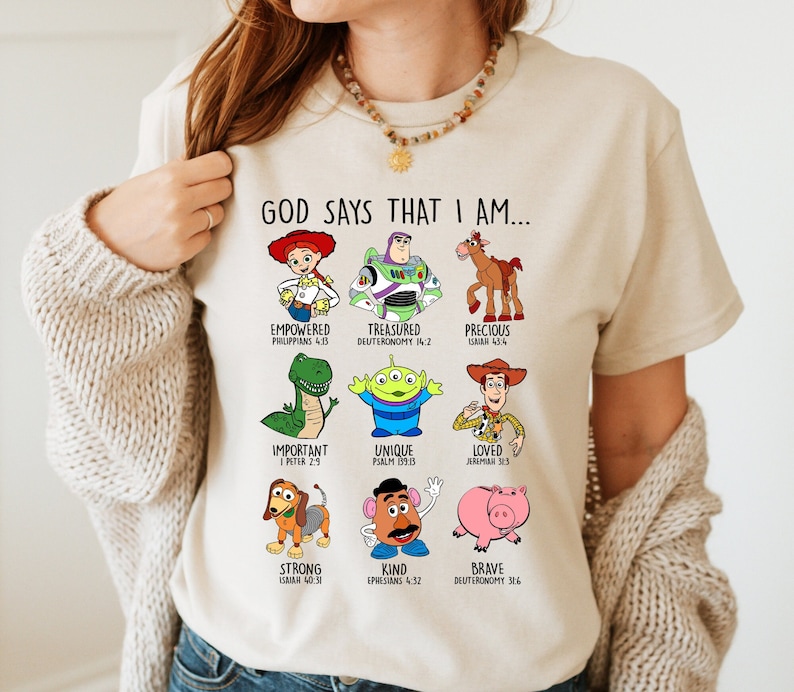 Peut inclure: Un t-shirt beige avec un graphique de personnages de Toy Story et des versets bibliques. Le texte dit "Dieu dit que je suis..." et liste les noms des personnages et les versets bibliques.