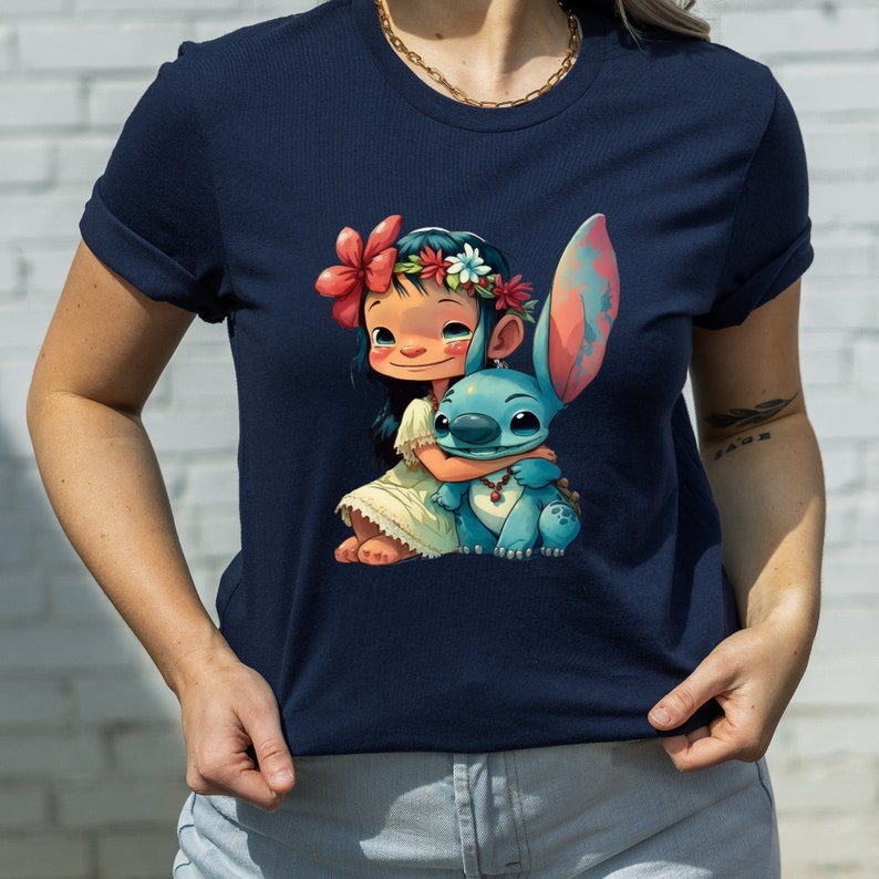 May include: A navy blue t-shirt with a cartoon image of a young girl with a flower crown hugging a blue alien character. The girl is wearing a white dress and the alien has red eyes and a red necklace.