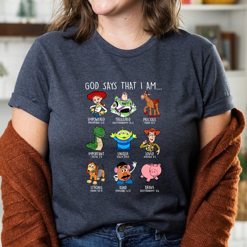 Peut inclure: Un t-shirt gris fonc&eacute; avec un motif repr&eacute;sentant des personnages de la franchise de films Toy Story. Le motif comprend le texte "Dieu dit que je suis..." et liste divers attributs positifs avec des versets bibliques correspondants.
