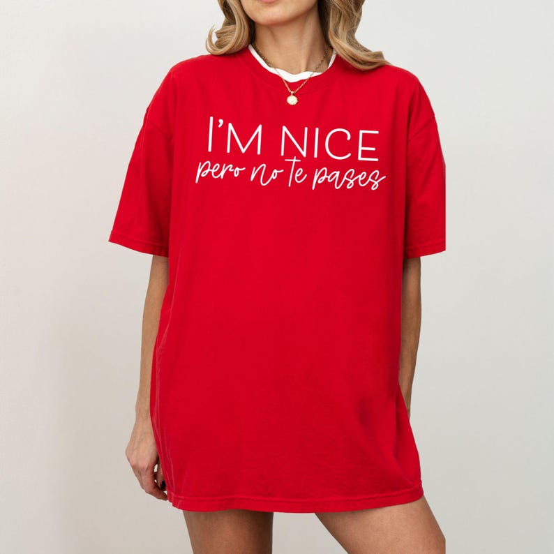 May include: A bright red short-sleeved t-shirt featuring the white text I'M NICE pero no te pases printed on the front. The shirt has a crew neckline and a relaxed fit, providing a simple and bold look with contrasting white lettering.