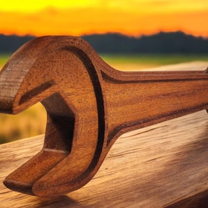 May include: A wooden wrench with a brown finish. The wrench is lying on a wooden surface with a blurred background of a sunset.
