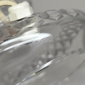 May include: Close-up of a clear glass object with a diamond-cut pattern. The object has a white plastic component attached to it, with a white cord. The word "Waterford" is faintly visible on the glass.