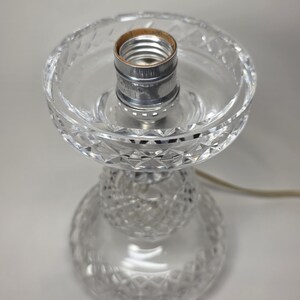 May include: A clear glass table lamp base with a decorative cut crystal design. The lamp base has a bulb socket and a power cord. The lamp base is approximately 8 inches tall.