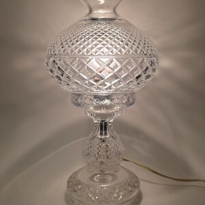 May include: A clear, cut-glass table lamp with a diamond pattern. The lamp has a bulbous globe shade, a flared top, and a round base. The lamp is approximately 14 inches tall.