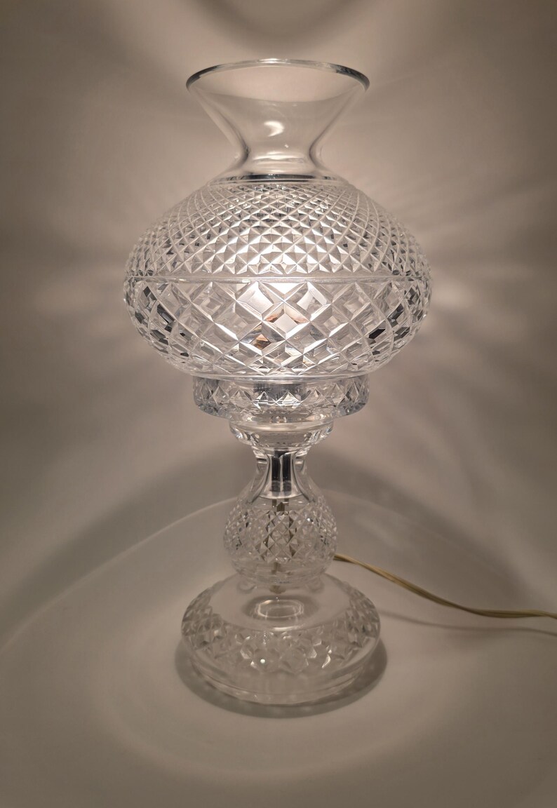 May include: A clear, cut-glass table lamp with a diamond pattern. The lamp has a bulbous globe shade, a flared top, and a round base. The lamp is approximately 14 inches tall.