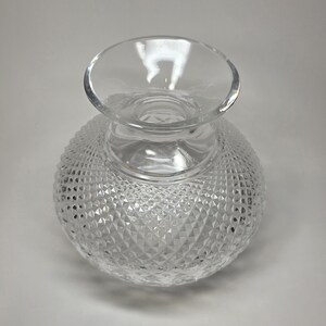 May include: A clear glass vase with a round, textured body and a flared top. The body of the vase is covered in a diamond pattern, creating a sparkling effect. The vase is likely used for decorative purposes.