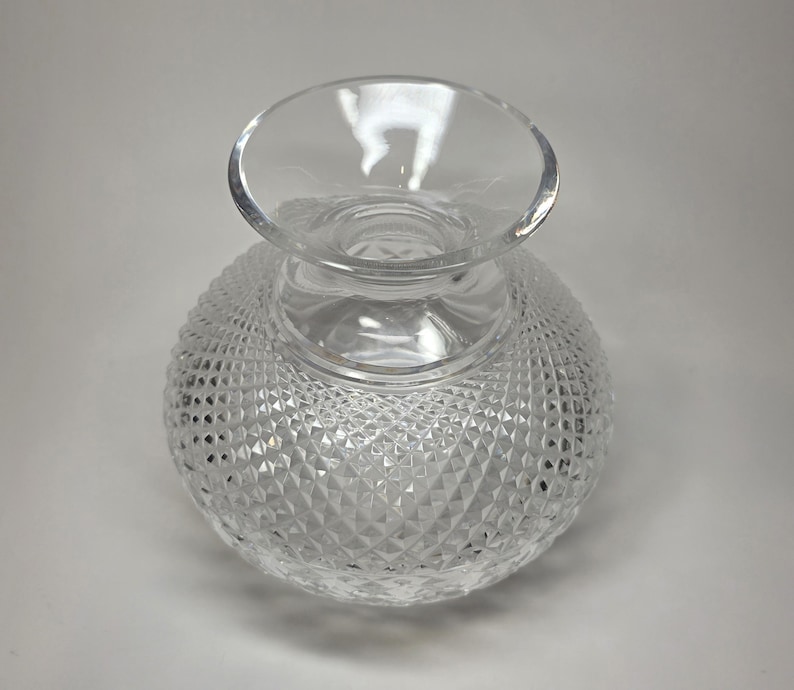May include: A clear glass vase with a round, textured body and a flared top. The body of the vase is covered in a diamond pattern, creating a sparkling effect. The vase is likely used for decorative purposes.