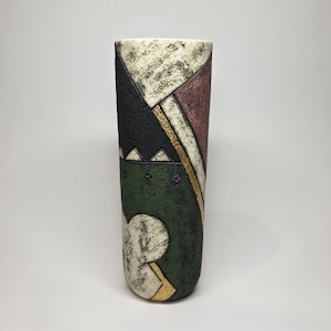 May include: A tall, cylindrical ceramic vase with a textured surface. The design features geometric shapes in black, red, green, and gold. The vase has a cream-colored top and a unique, artistic aesthetic.