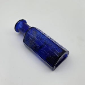 May include: A deep blue antique glass bottle with a hexagonal design. The bottle has a rounded neck and the text "NOT TO BE TAKEN" and "USE WITH CAUTION" is embossed on the side.