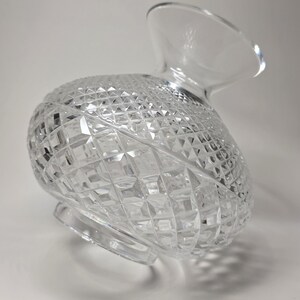 May include: Clear crystal pitcher with a diamond-cut pattern. The pitcher has a rounded body and a flared spout. The base is a circular shape. The pitcher is made of glass and is designed to hold liquids.