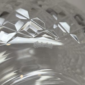 May include: Close-up of a clear glass object with a diamond-cut pattern. The glass has a reflective surface, and the word "Waterford" is etched into the glass. The object appears to be a decorative bowl or vase.