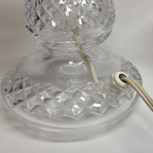 May include: Clear glass table lamp with a diamond-cut pattern on the base and globe. The lamp has a white electrical plug and a cream-colored cord. The lamp is designed for indoor use.