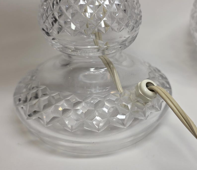 May include: Clear glass table lamp with a diamond-cut pattern on the base and globe. The lamp has a white electrical plug and a cream-colored cord. The lamp is designed for indoor use.